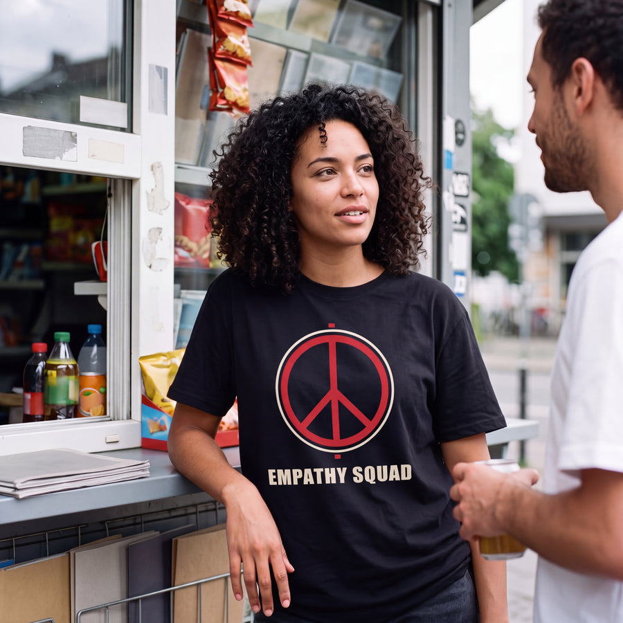 KI-erstellte Produktvisualisierung: Frau am Kiosk trägt das schwarze Empathy Squad Peace T-Shirt mit rot-cremefarbenem Frontprint.