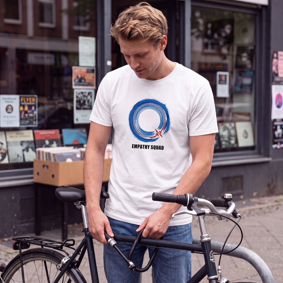 KI-generierte Produktvisualisierung: Mann im weißen Empathy-Squad-Pinselkreis-Blau-T-Shirt vor einem Plattenladen, mit blauem Frontmotiv, rotem Akzent und EMPATHY SQUAD.