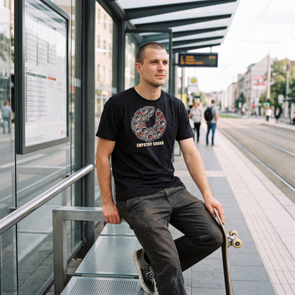 KI-Produktvisualisierung: Mann mit Skateboard an einer Haltestelle im schwarzen Empathy Squad Rasterkreis T-Shirt; Lautsprecherkreis mit roten Akzenten und Markenname oben auf der Brust.