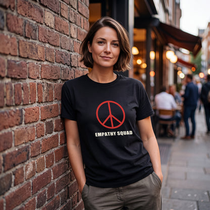 Frau vor einer Backsteinwand im schwarzen Empathy-Squad-T-Shirt. Das vollständige rote Peace-Zeichen und EMPATHY SQUAD sitzen auf der Brust.